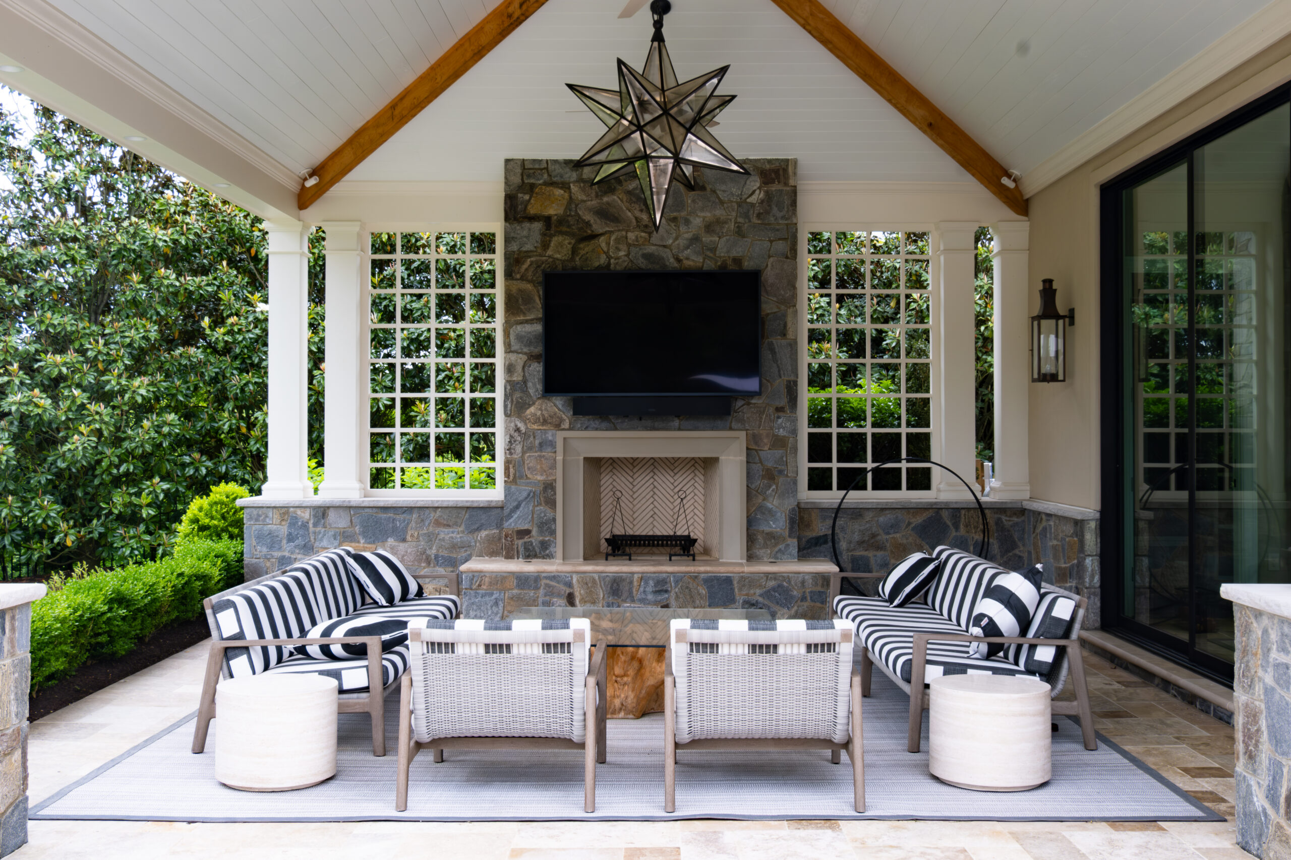 Covered outdoor living space with stone fireplace, mounted TV, and vaulted ceiling at Hunter Mill Residence by McHale Landscape Design