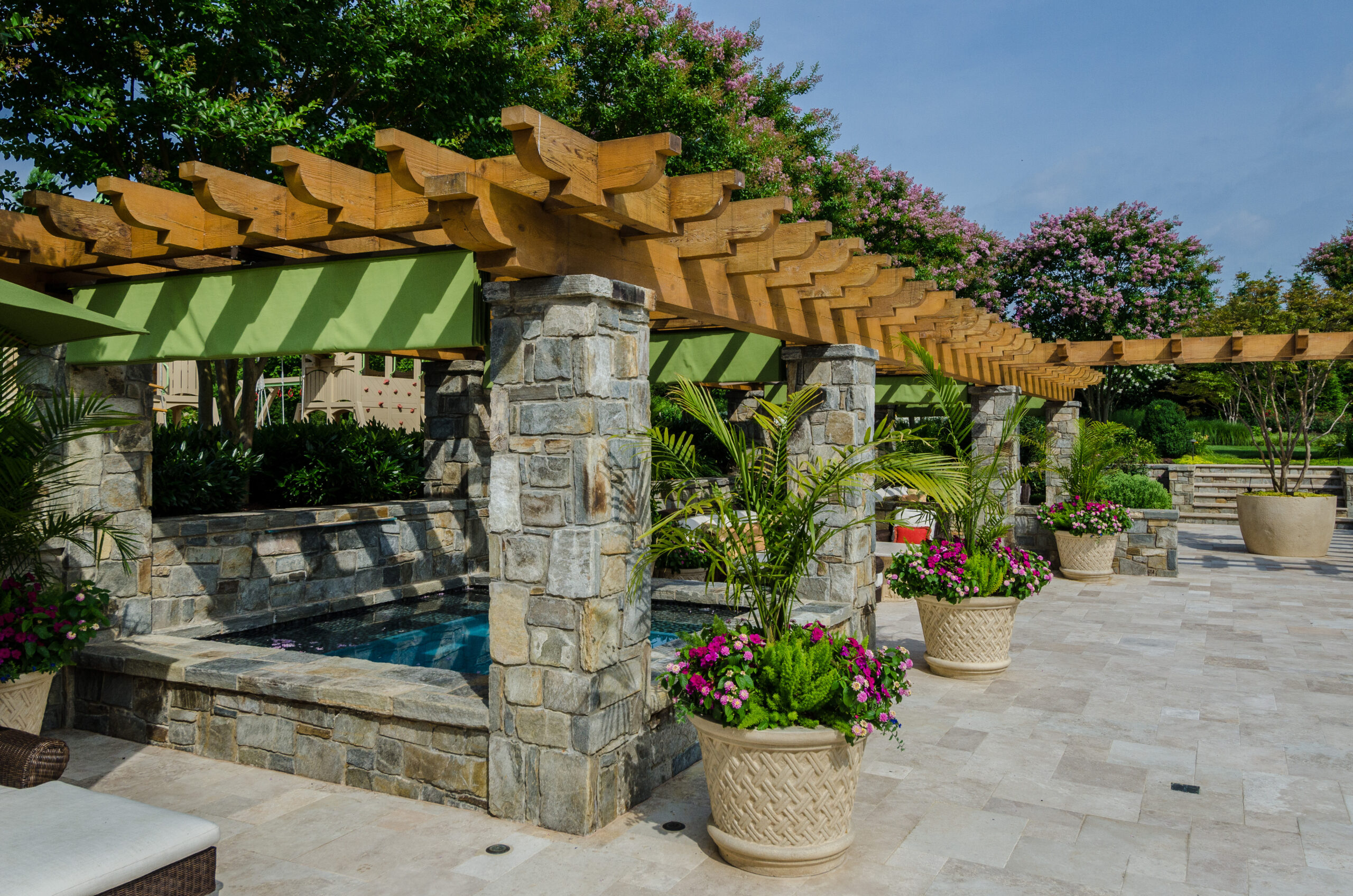 Stone pergola with wood timber beams, retractable canopy, pool, and container plantings designed by McHale Landscape Design